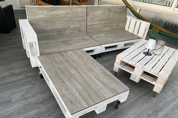 Paletten-Lounge aus Europaletten im Außenbereich, auf Rücken- und Sitzflächen befinden sich Fliesen in dunklerer Holzoptik, in denen unsichtbare Infrarot-Heizelemente verbaut sind.