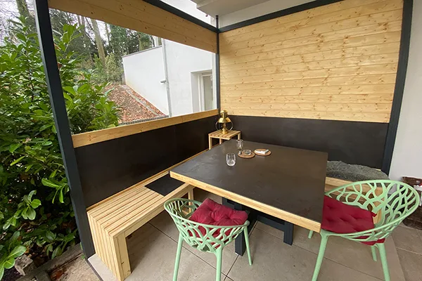 windgeschützte und beheizte Outdoor-Lounge, stilvoll in Holz und Schwarz. Als Farbakzent dienen zwei grüne Sesselstühle mit roten Kissen.